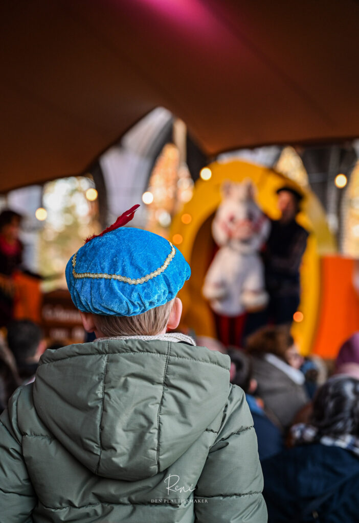 Kind met blauwe feestmuts kijkt naar een Sinterklaasvoorstelling