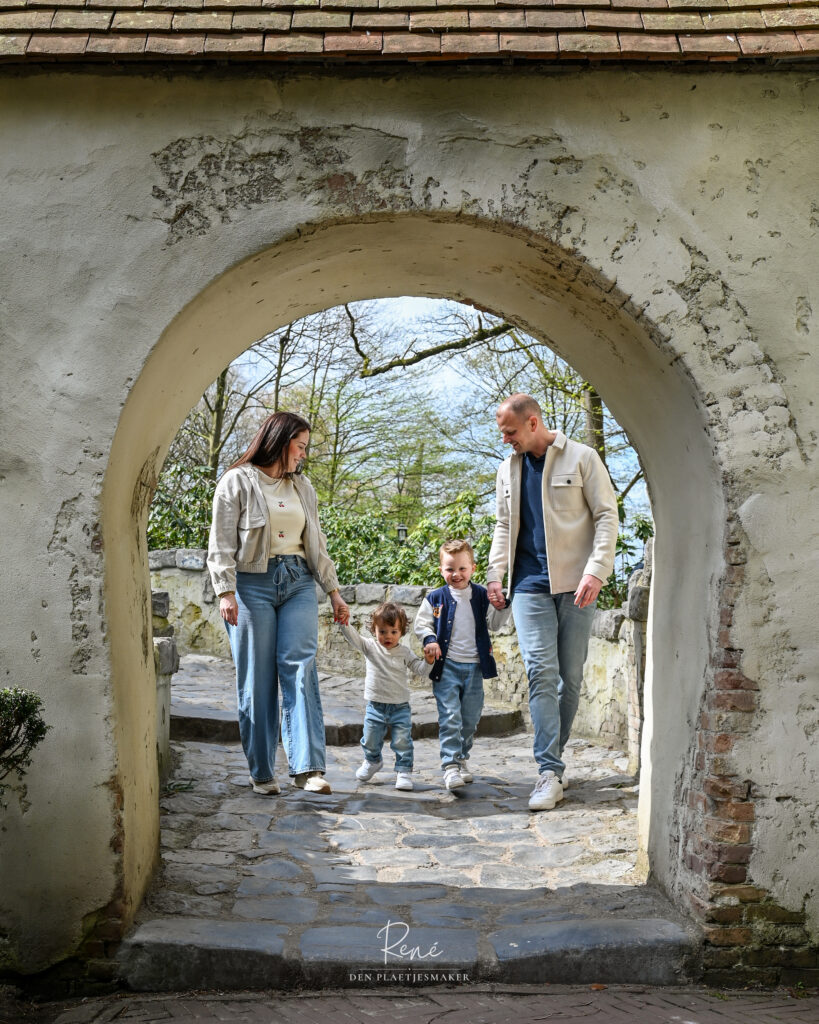 Gezin met twee kinderen loopt samen door een stenen poort tijdens een fotoshoot