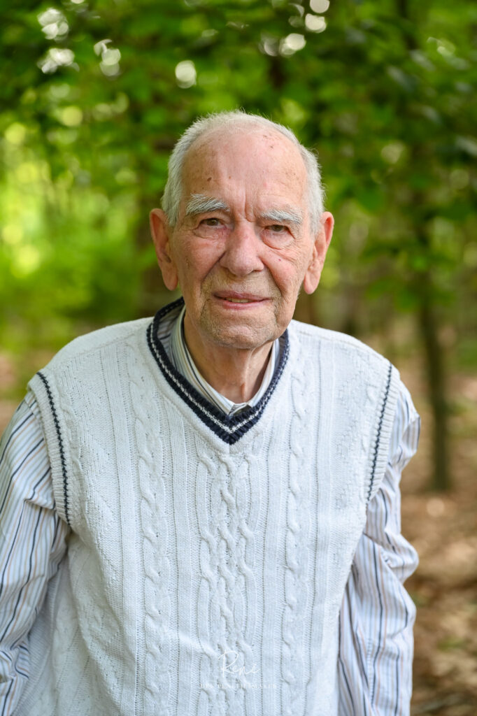 Oudere man in een witte trui tijdens een portretshoot in het bos